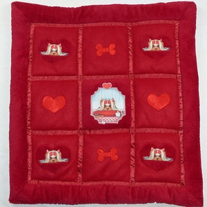 Könnte beinhalten: Rotes gestepptes Hundebett mit einem Knochen und einem Hundegesicht in der Mitte. Das Bett ist in neun Quadrate mit verschiedenen Bildern in jedem Quadrat unterteilt.