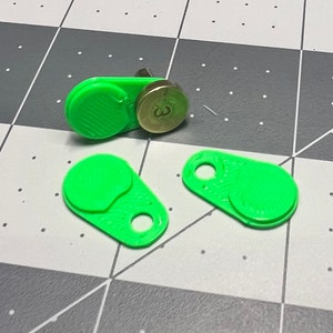 May include: Three green plastic keychains with a round, raised button on each. One keychain has a small, round, brass-colored button with a number "3" on it.