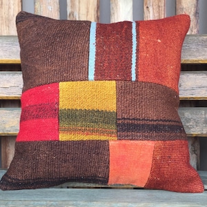 Può includere: Un cuscino patchwork con una varietà di colori e trame, tra cui rosso, arancione, giallo, marrone e blu. Il cuscino è realizzato in tessuto tessuto e ha una forma quadrata.