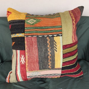 May include: A colorful patchwork pillow with a variety of woven patterns in shades of red, orange, yellow, green, and black. The pillow is made from recycled materials and has a unique, handmade look.