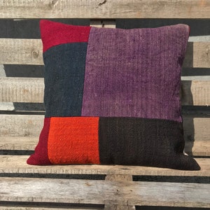 May include: A square pillow with a patchwork design. The pillow is made of four different fabrics in shades of red, purple, orange, and black.