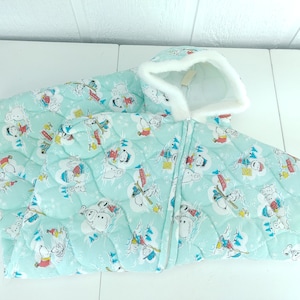 Puede incluir: Un saco de dormir de color azul claro con capucha y forro de piel sintética blanca. El saco de dormir está acolchado y presenta un patrón repetido de personajes de dibujos animados patinando sobre hielo y jugando en la nieve.