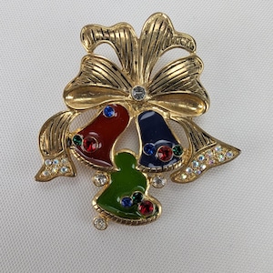 May include: A gold-tone Christmas brooch featuring three bells with red, blue, and green enamel and rhinestones. The bells are tied together with a gold bow.
