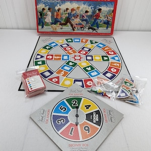May include: A vintage board game called "Trivial Pursuit for Juniors". The game includes a game board, a spinner, and cards. The game board is circular and has a colorful design. The spinner is a circular wheel with numbers 1 through 9. The cards are red and have a white border.