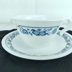 Puede incluir: Una taza de té y un platillo blancos con un patrón floral azul. La taza tiene un asa y el platillo tiene un borde festoneado.