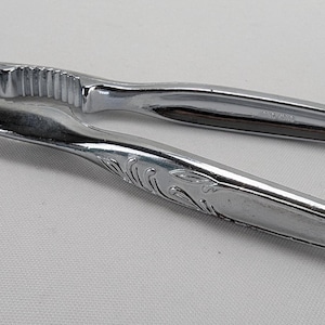 Puede incluir: Un cascanueces de plata con un diseño decorativo en el mango. El cascanueces tiene un borde dentado para romper nueces.