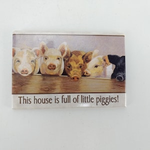 Op de afbeelding: Een magneet met een afbeelding van vijf biggetjes die over een houten hek kijken. De tekst "This house is full of little piggies!" staat onder de afbeelding.
