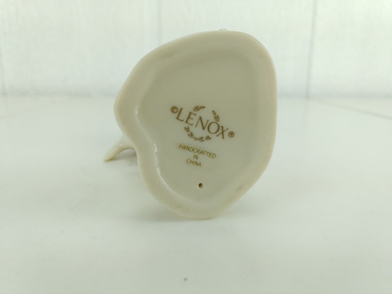 May include: The bottom of a white porcelain figurine with the words "LENOX" and "HANDCRAFTED IN CHINA" in gold lettering.