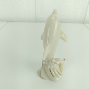 May include: A white porcelain figurine of a dolphin leaping out of the water. The dolphin is detailed with gold accents and is set on a base with a wave design.
