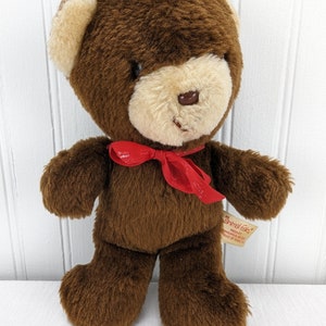 May include: Brown teddy bear with a red bow tie. The bear has a beige face and a tag that reads "Animal Fair" with the text "Product of Korea" underneath.
