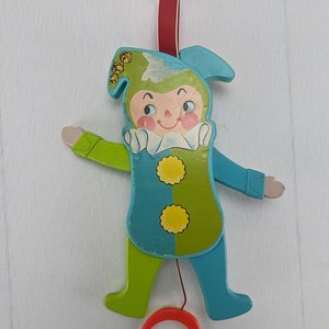 May include: A vintage pull-string toy of a jester with a blue and green costume. The jester has a red string attached to its hand and a red ring at the bottom of the string.