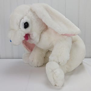 May include: White plush bunny rabbit toy with pink ears and blue eyes. The bunny is sitting on a white surface.