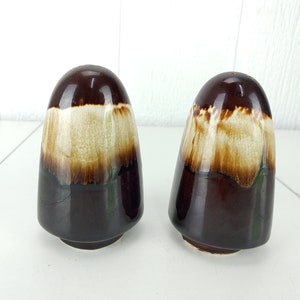 Puede incluir: Un juego de dos saleros y pimenteros de cerámica marrón y blanco. Los saleros tienen forma de cono redondeado y están cubiertos con un esmalte marrón con una banda blanca alrededor del medio.