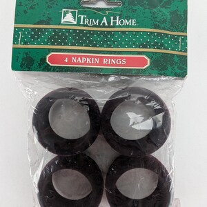 Può includere: Confezione di quattro anelli per tovaglioli neri. La confezione è etichettata "Trim A Home" e "4 Napkin Rings".