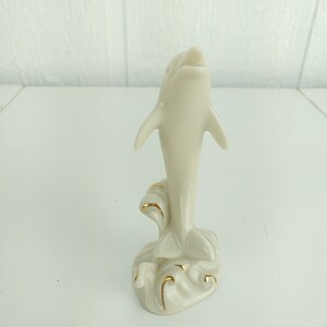 May include: A white porcelain figurine of a dolphin leaping out of the water. The dolphin is painted with gold accents and is set on a base with waves.