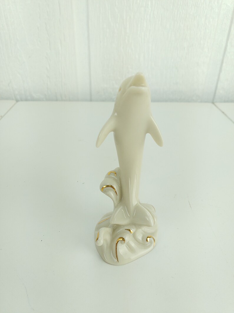 May include: A white porcelain figurine of a dolphin leaping out of the water. The dolphin is painted with gold accents and is set on a base with waves.