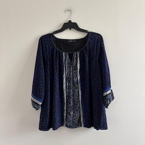 May include: A long-sleeve blouse featuring a black and blue animal print pattern. The garment has a scoop neckline, a central vertical panel with a distinct speckled design, and blue and white striped accents on the cuffs and front panel.