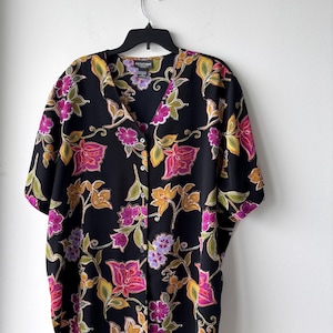 May include: A black button-up shirt with a floral print in shades of pink, yellow, and green. The shirt has a v-neck and short sleeves. The label reads "Notations".