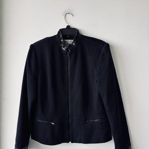 May include: A black blazer with a sequined collar and cuffs. The blazer has a zipper closure and two pockets.