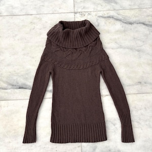 May include: A brown, long-sleeved sweater with a cowl neck. The sweater features a cable knit design around the neck and a ribbed hem and cuffs. The garment is made of a soft, knitted material.