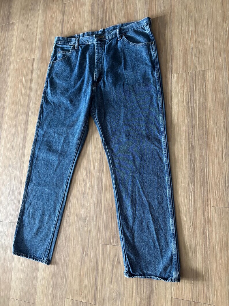 May include: A pair of blue denim jeans with a classic five-pocket design. The jeans have a straight leg cut and a button and zipper closure. The denim has a medium wash with subtle fading and wear.