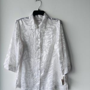 May include: White button-down shirt with a floral pattern. The shirt has a collar and three-quarter sleeves.