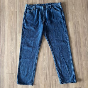 May include: A pair of classic blue denim jeans. The jeans have a straight leg cut, five-pocket design, and a button and zipper closure. The denim has a medium wash with subtle fading and wear.