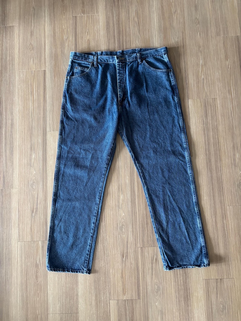 May include: A pair of classic blue denim jeans. The jeans have a straight leg cut, five-pocket design, and a button and zipper closure. The denim has a medium wash with subtle fading and wear.