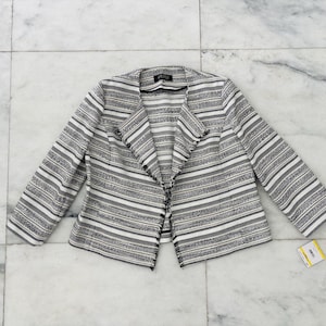 May include: A black, white, and gray striped blazer with long sleeves. The open-front jacket has a notched collar and a textured fabric. A price tag is visible on the lower right. The blazer is a women's clothing item.