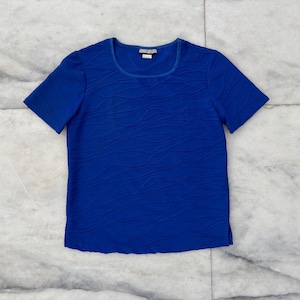 Könnte beinhalten: Ein kurzärmliges, königsblaues Oberteil mit einem strukturierten Wellenmuster. Das Shirt hat einen quadratischen Ausschnitt und ein kleines Etikett am Hals. Das Kleidungsstück ist aus leichtem Material gefertigt.