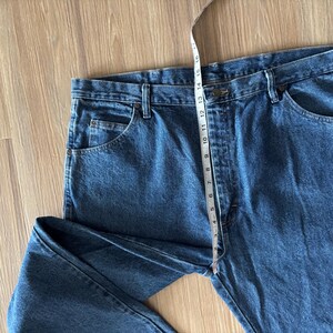 May include: Blue denim jeans with a straight leg design. A measuring tape is placed across the waist, showing a measurement of approximately 16 inches. The jeans have classic five-pocket styling.