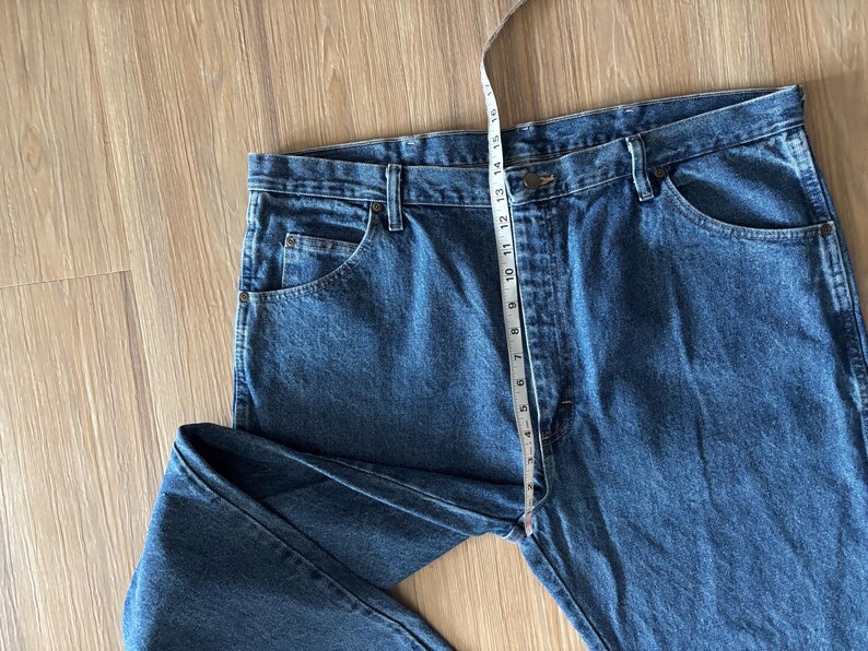 May include: Blue denim jeans with a straight leg design. A measuring tape is placed across the waist, showing a measurement of approximately 16 inches. The jeans have classic five-pocket styling.