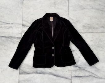 Op de afbeelding: Een zwarte fluwelen blazer met een revers, sluiting met twee knopen en twee voorzakken. De jas heeft lange mouwen en een getailleerde pasvorm. De voering is lichtroze. De blazer wordt gepresenteerd op een marmeren oppervlak.