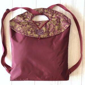Peut inclure: Un sac à dos bordeaux avec un rabat à motif floral doré et un logo "Bag Spirit". Le sac à dos a des bretelles réglables.