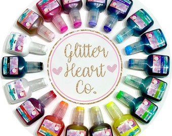 May include: A circle of 16 small bottles of glitter glue in various colors, including pink, blue, green, yellow, orange, and purple. The bottles are arranged in a circle around a white circle with the text "Glitter Heart Co." in gold lettering.