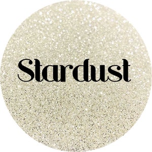 May include: A circular image of sparkling, iridescent glitter. The glitter is a light, neutral color, with the word "Stardust" in a bold, black font across the center. The glitter appears to be finely milled.