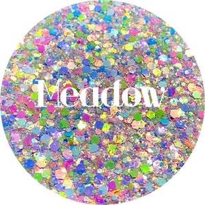 May include: A close-up of iridescent glitter in a variety of colors, including pink, blue, green, and yellow. The glitter is arranged in a circular pattern and the word "Meadow" is written in white letters in the center.