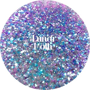 May include: A close-up of iridescent blue, purple, and white glitter. The glitter is in a round container and the text "Lunar Moth" is visible in the center of the image.