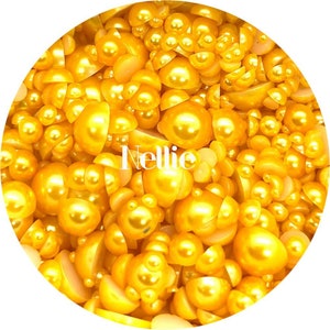 May include: A close-up image of a large quantity of gold pearl beads. The beads are a mix of full and half pearls, and they are all shiny and reflective.