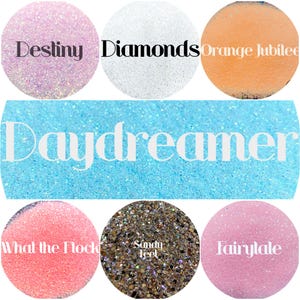 May include: A collection of seven circular glitter samples and one large rectangular glitter sample. The colors include light pink labeled Destiny, white labeled Diamonds, orange labeled Orange Jubilee, light blue labeled Daydreamer, bright pink labeled What the Flock, brown and gold labeled Sandy Feet, and soft pink labeled Fairytale.