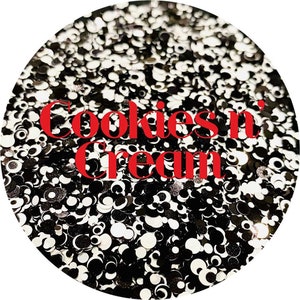 May include: Circular image filled with black, white, and silver glitter. The glitter pieces are in various shapes and sizes. Bold red text in the center reads "Cookies n' Cream".