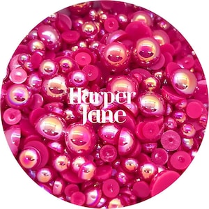 May include: A close-up image of a variety of pink iridescent and solid pink round and flat cabochons. The cabochons are scattered on a white background. The text "Harper Jane" is visible in the center of the image.