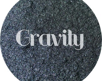 May include: A close-up of a dark gray, sparkly, textured surface with the word "Gravity" printed in white.