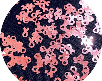 May include: Pink glitter confetti in the shape of a ribbon. The confetti is scattered on a black background.