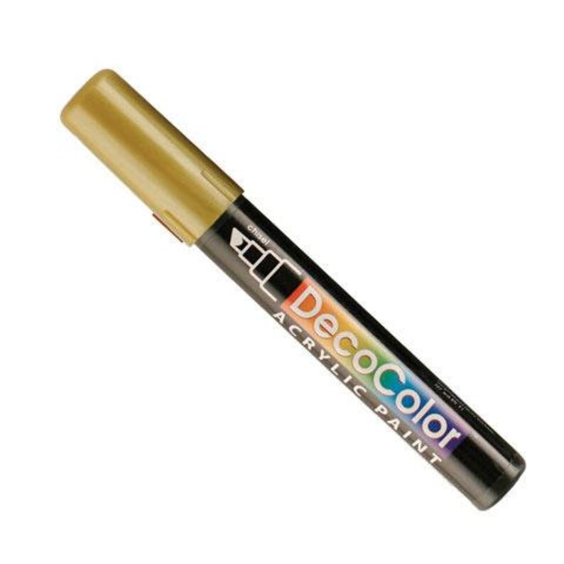 May include: A gold-colored DecoColor acrylic paint marker with a chisel tip. The marker has a black barrel with the DecoColor logo and the words "Acrylic Paint" printed on it. The marker is designed for art projects.