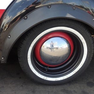 May include: Close-up of a car wheel with a black tire, a red hubcap, and a chrome center. The wheel has a white stripe around the edge. The car's black fender is visible above the wheel.