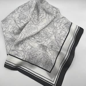 May include: A white square scarf with a black floral pattern. The scarf has a black border with two thin black stripes. The floral design features large peony blooms and leaves.