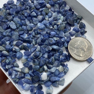 May include: A small white box filled with blue and white tumbled stones. The stones are about the size of a quarter, which is shown in the image for scale.