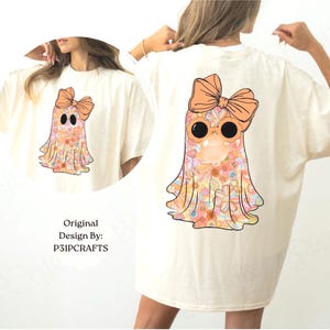 K&ouml;nnte beinhalten: Ein cremefarbenes T-Shirt mit einer Grafik eines Geistes mit Blumenmuster, der eine gro&szlig;e orangefarbene Schleife und eine runde Sonnenbrille tr&auml;gt und eine Kaugummiblase bl&auml;st. Der Text Original Design By: P31PCRAFTS steht unter dem Geist.