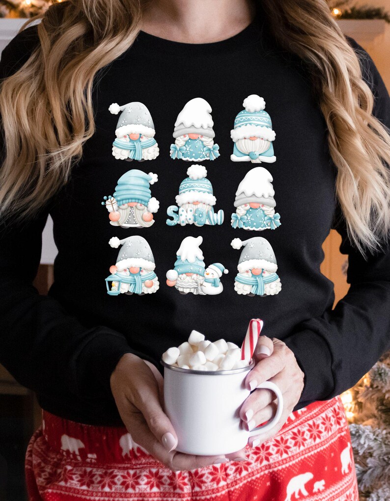 May include: A black long-sleeve shirt featuring a graphic print of nine individual gnomes in various winter outfits. The gnomes are colored in shades of light blue, white, and gray. One gnome holds a sign that says SNOW in light blue letters.